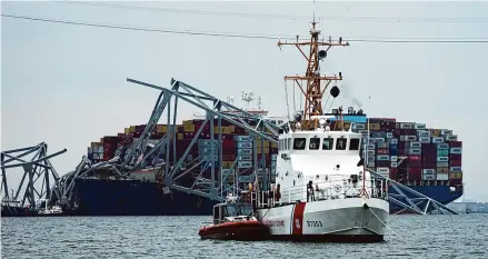  ?? ?? A Coast Gaurd cutter patrols in front of a cargo ship that is stuck under the part of the structure of the Francis Scott Key Bridge after the ship hit the bridge on Wednesday in Baltimore, Md.