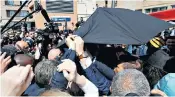  ?? ?? Mr Macron hurries away from the scene in the Paris suburbs after sheltering under the special Kevlar umbrella