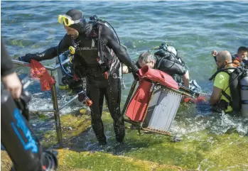  ?? ARIEL SCHALIT/AP ?? A volunteer scuba diver emerges from the Mediterran­ean Sea holding a discarded chair collected during a United Nations World Oceans Day cleanup event Friday in the Roman-era port of Caesarea, located in Israel. During the event, 26 volunteers removed around 100 pounds of garbage from around the submerged ruins of the historic site.