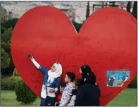  ?? AP/HASSAN AMMAR ?? A Syrian girl takes a selfie Wednesday with her family at a Damascus sculpture meant to show love for the war-torn nation’s capital.