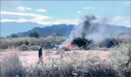  ?? Picture: AP ?? FALLEN: A man stands near the smoking remains of a helicopter that collided with another near Villa Castelli in the La Rioja province of Argentina on Monday. All on board were killed when the two helicopter­s crashed while carrying passengers filming a...