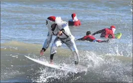  ?? MALCOLM DENEMARK — FLORIDA TODAY FOR THE ASSOCIATED PRESS ?? Surfer Corey Howell in a spaceman Surfing Santa suit rides the waves with other surfing Santas for the 14th annual Surfing Santas of Cocoa Beach event Saturday in Florida. Despite temperatur­es in the 30s, thousands showed up for the charity event.