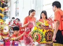  ??  ?? Huang Qingliang (right), Qin Jinmin (second right) and Qiu Haiwei (left) paint a lion head following the guidance of a craftswoma­n in the school.