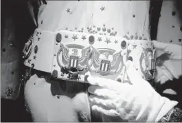  ??  ?? Archivist Dee Dee Antle adjusts the belt buckle of Elvis Presley’s famous American Eagle jumpsuit. Costumes including two-piece karate-type ensembles and one-piece jumpsuits are on display.