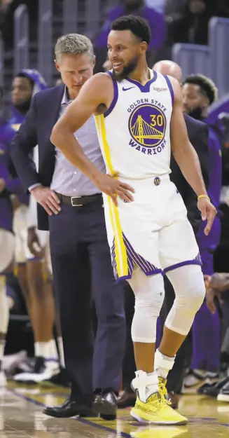  ?? Ben Margot / Associated Press ?? Warriors guard Stephen Curry, with head coach Steve Kerr, awkwardly holds his left hand, which would prove to be broken after a collision with Phoenix’s Aron Baynes.