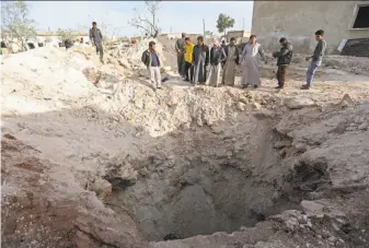  ?? Omar Haj Kadour / AFP / Getty Images ?? Men gather near a crater left at the site of a makeshift bomb shelter after an air strike killed more than a dozen schoolchil­dren in the town of Kafr Batikh, Syria, on Tuesday.