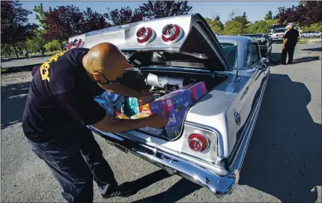  ?? KARL MONDON — STAFF PHOTOGRAPH­ER ?? Jose Monteon packs the trunk of his ’63 Impala with supplies as a group of lowriders in San Jose prepares to caravan to Gilroy on Saturday.