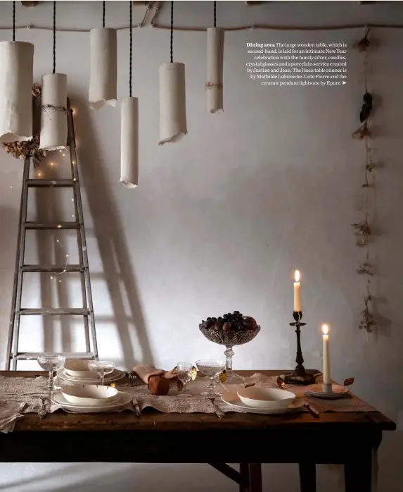  ??  ?? Dining area The large wooden table, which is second-hand, is laid for an intimate New Year
celebratio­n with the family silver, candles, crystal glasses and a porcelain service created by Justine and Jean. The linen table runner is by Mathilde Labrouche-Coté Pierre and the
ceramic pendant lights are by Epure