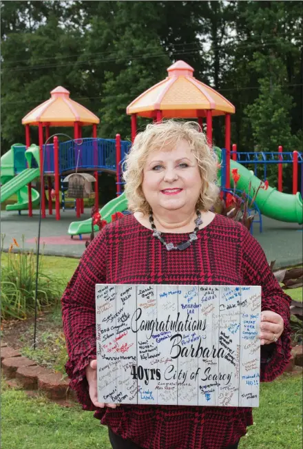  ?? MARK BUFFALO/THREE RIVERS EDITION ?? Barbara Hubach, office manager for the Searcy Parks and Recreation Department, holds a board signed by city employees marking her 40th anniversar­y with the department. Hubach started working for the Parks Department in May 1979 under former director Harry Miller.