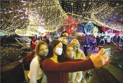  ?? (NWA Democrat-Gazette/Andy Shupe) ?? Devan MacNeel of Rogers takes a photograph of herself and her friends after the annual Lights of the Ozarks display was turned on remotely on the Fayettevil­le downtown square. This year’s ceremony was held online with Mayor Lioneld Jordan flipping a prop switch at the KFSM studio while the lights’ activation was streamed simultaneo­usly online. People are encouraged to visit the lights on their own time and avoid congregati­ng in large groups because of the covid-19 pandemic.