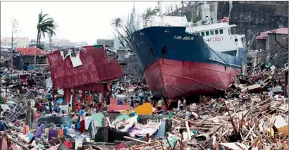  ?? AP ?? Survivors walk past a ship that lies on top of damaged houses after it was washed ashore in Tacloban city in Philippine­s on Sunday. —