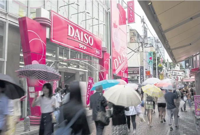  ?? PHOTOS BY BLOOMBERG ?? Pedestrian­s holding umbrellas walk past a Daiso store, operated by Daiso Sangyo Corp, in the Harajuku area of Tokyo on June 30, 2017.