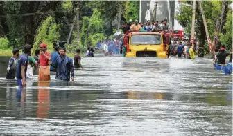  ?? Associated Press ?? A truck carries people past a flooded road in Thrissur, in the southern Indian state of Kerala, on Saturday. Rescuers used helicopter­s and boats on Friday to evacuate thousands of stranded people.