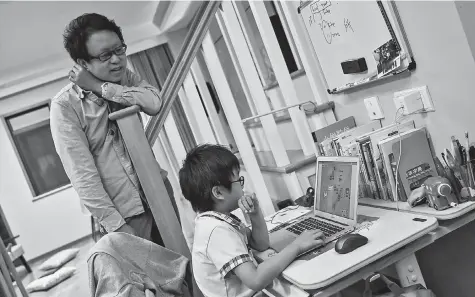  ??  ?? Zhou Ziheng (left) helps his son Vita create a game with coding on his laptop at their home in Shanghai. — AFP