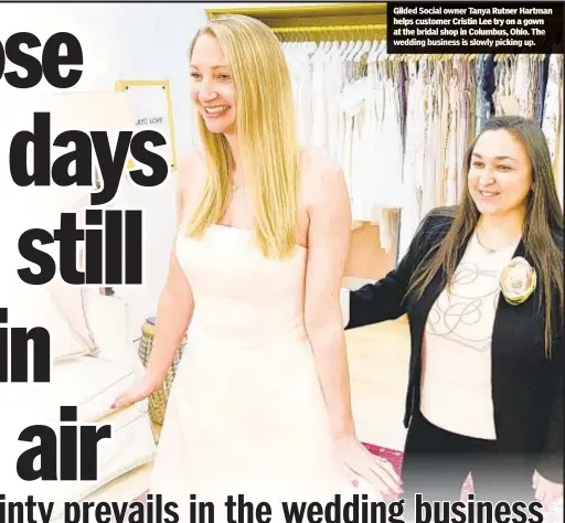  ??  ?? Gilded Social owner Tanya Rutner Hartman helps customer Cristin Lee try on a gown at the bridal shop in Columbus, Ohio. The wedding business is slowly picking up.