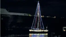  ??  ?? A boat sails past spectators during the Boat Parade of Lights in the Welland Canal during the 39th annual Canal Days Marine Heritage Festival Sunday.