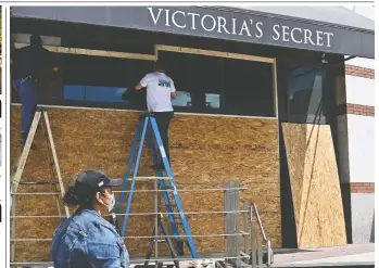  ?? ANGELA WEISS/AFP VIA GETTY IMAGES ?? Workers board up a Victoria’s Secret store front Monday in New York City after a night of protest over an officer’s killing of George Floyd, an African-American man in Minneapoli­s.