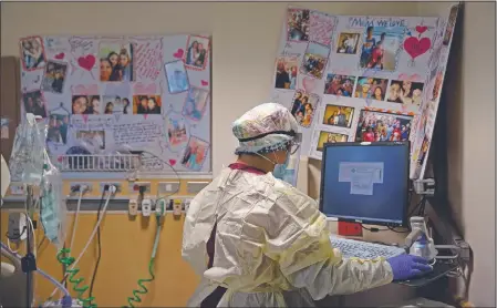  ??  ?? Nurse Sarvnaz Michel works on a computer while assisting a covid-19 patient in a room with poster boards filled with family photos and get-well messages at St. Jude Medical Center. The 28-year-old’s career has forced her to blur and blend her two lives. She agonizes over her every move in the hospital — “Did I put my gear on the right way, did I take it off the right way, did I touch something wrong accidental­ly?” — and locks her shoes in the car after her shifts.