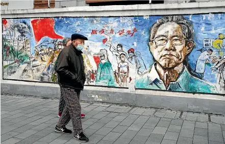  ?? AP ?? Wuhan residents wearing masks pass a mural titled ‘‘Memories’’ on the eve of the first anniversar­y of the city’s lockdown after the Covid-19 coronaviru­s was first detected there. The mural includes a depiction of Chinese medical expert Dr Zhong Nanshan, who refuted the official Chinese government line downplayin­g the severity of the crisis, and revealed that the virus is transmissi­ble between people.