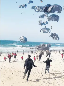  ?? Picture: AFP ?? DROPPING IN. Palestinia­ns run towards parachutes attached to food parcels, air-dropped from US aircraft on a beach in the Gaza Strip on Saturday.
