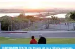  ?? — AFP ?? HUNTINGTON BEACH, CA: People sit on a hillside overlookin­g oil pumpjacks at the Huntington Beach Oil Fields amidst the coronaviru­s pandemic on Monday in Huntington Beach, California.