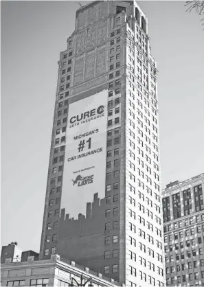  ?? JUNFU HAN/DETROIT FREE PRESS ?? A Cure Auto Insurance advertisem­ent hangs on the Broderick Tower in Detroit on Monday in place of Robert Wyland’s painting of three humpback whales.