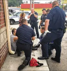  ?? KATIE WEDELL / STAFF ?? Dunkin (kneeling) and other first responders talk to a man who was just revived from a heroin overdose at a gas station on Keowee Street on June 12.