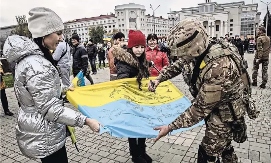  ?? FINBARR O’REILLY PARA THE NEW YORK TIMES ?? Los residentes de Jersón celebraron durante días, después de que su ciudad fue liberada. Un soldado ucraniano firma una bandera.