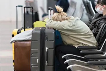  ?? AP Photo/Alex Brandon ?? ■ Jessica Andrijausk­as, from Buenos Aires, Argentina, rests her head on her luggage as she awaits the results of her COVID19 test Wednesday at Ronald Reagan Washington National Airport in Arlington, Va. Winter weather and crew members infected with COVID-19 have forced airlines to spike thousands of U.S. flights last week, complicati­ng travel plans for many people during the busy holiday season. It’s not clear when travel will return to normal, but airlines say a recent move by U.S. public health officials should help get workers back sooner.