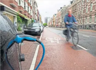  ?? GETTY ?? Un ciclista circula por un carril bici, delante de un coche eléctrico en recarga.