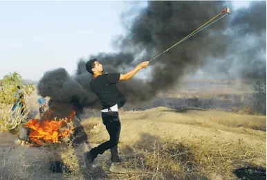  ??  ?? A PALESTINIA­N USES a sling to hurl rocks at Israeli troops near the Gaza border yesterday.