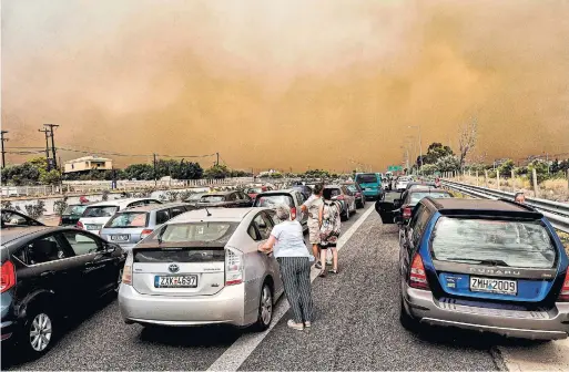  ?? VALERIE GACHE/AFP/GETTY IMAGES ?? Cars are blocked at the closed National Road during a wildfire in Kineta, near Athens, on Monday. Fuelled by 80 km/h winds, the fires cut off escape routes.