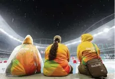  ??  ?? Olympic volunteers sit in the rain during the Rio Games. Many volunteers quit after working long hours with little food.