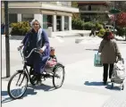  ??  ?? A woman carries a child
on a threewheel bicycle
as another one pulls her trolley basket near an open
air fruit and vegetable market in Athens, April 24. (AP)