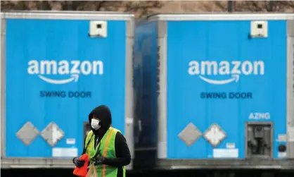  ??  ?? A worker in a face mask walks by trucks parked at an Amazon facility in Bethpage on Long Island, New York, on Tuesday. Photograph: Andrew Kelly/Reuters