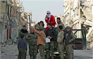  ?? — AP ?? Iraqi security forces take a picture with a man wearing a Santa Claus suit amid houses and shops destroyed during the war to liberate Mosul from Daesh militants.