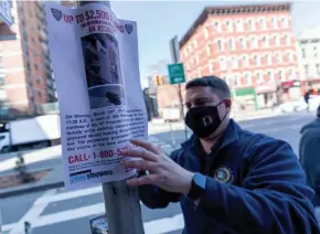  ?? MARY ALTAFFER/AP ?? A police officer hangs a sign Tuesday offering a reward for informatio­n on the person who attacked an Asian American woman in Manhattan a day earlier.