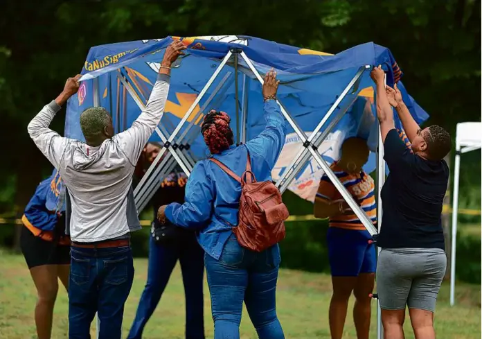  ?? JOHN TLUMACKI/GLOBE STAFF ?? A group of people worked together to set up a tent Saturday to protect them from the rain during the picnic at Franklin Park.