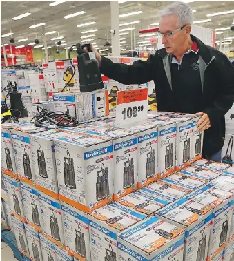  ?? DAN JANISSE ?? Canadian Tire general manager Phil Giacalone put in a special emergency response order for sump pumps, mops and fans. Customer Richard Raymond checks out a pump at the east Windsor location on Friday.