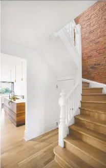  ?? ADRIEN WILLIAMS PHOTOS, COURTESY OF MICROCLIMA­T ARCHITECTU­RE ?? The stairway with its traditiona­l banisters and the brick wall are part of the charm of the existing home, while the kitchen beyond the entry hall is part of Quartier House’s contempora­ry new interior.