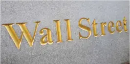  ??  ?? NEW YORK: A sign for Wall Street is carved into a building located near the New York Stock Exchange on Friday. Solid, if uninspirin­g, US stocks veered lower in early trading on Friday as investors pored through earnings from General Electric,...