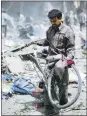  ?? SAMEER ALDOUMY/GETTY IMAGES ?? A Syrian man carries a bike through the rubble Sunday after airstrikes by Syrian government forces on a marketplac­e in Douma.