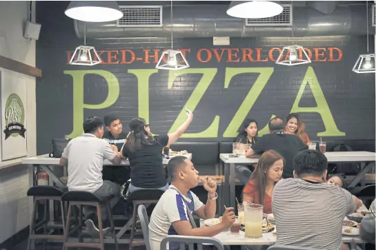  ?? PHOTOS BY BLOOMBERG ?? A customer uses a smartphone to take a selfie as other diners eat at a Greenwich Pizzeria, operated by Jollibee Foods Corp, in Manila.