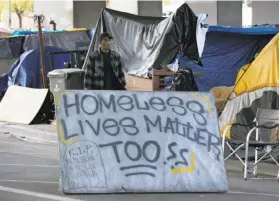  ??  ?? Right: Shawn Moses walks behind the sign he created at a homeless encampment on Northgate Avenue, where he has lived for about three years.