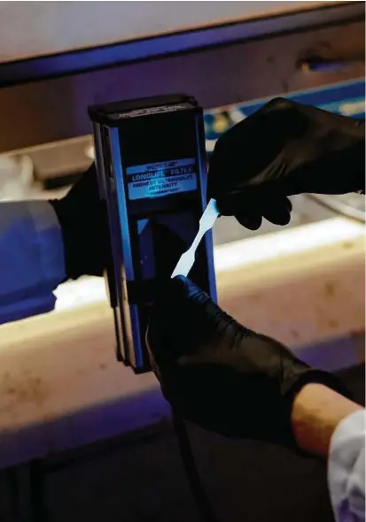  ?? Lyndon French photos / The New York Times ?? Dr. Adam Feinberg places a plastic sample under ultraviole­t light, in Urbana, Ill. Scientists are developing new plastics that, when prompted, self-destruct for reuse.