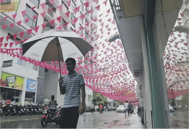  ??  ?? A man down a street decorated with flags of the Maldivian president Yameen Abdul Gayoom’s Progressiv­e Party of Maldives in Male