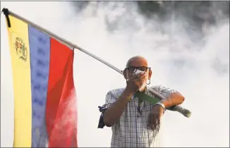  ?? Boris Vergara / Associated Press ?? An opponent to Venezuelan President Nicolas Maduro carrying a Venezuelan flag covers his face amid tear gas fired by soldiers loyal to Maduro during an attempted military uprising to oust Maduro in Caracas, Venezuela, on Tuesday.