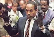  ?? ?? O.J. Simpson, wearing the blood-stained gloves found by Los Angeles Police and entered into evidence in Simpson's murder trial, displays his hands to the jury at the request of prosecutor Christophe­r Darden in this file photograph from June 15, 1995, as his attorney Johnnie Cochran Jr., right, looks on.