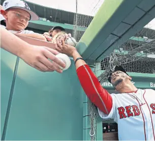  ?? JIM DAVIS GETTY IMAGES ?? Red Sox star Mookie Betts has to reach around the new protective netting to sign some autographs before the start of a game in Boston. The safety measure is popular with players.