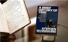  ?? Daniel Leal-Olivas/AFP ?? Cadeira de rodas usada por Stephen Hawking nos anos 1980 e 1900 e uma cópia de seu livro “Uma Breve História do Tempo” assinada por ele